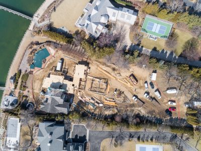 Aerial view of early excavation and sitework on a cleared lot surrounded by bare trees