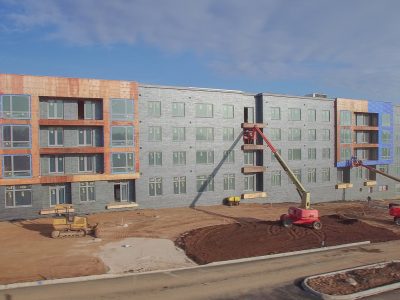 Four-story multifamily building in framing and sheathing stage with sitework out front
