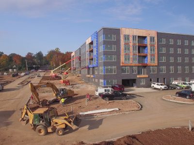 Excavator grading in front of a multifamily building under construction