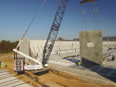 Crawler crane lifting a concrete wall panel into position as workers guide it