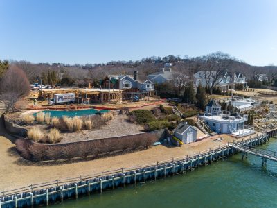 Wide drone aerial of a waterfront property mid-construction with pool and shoreline visible