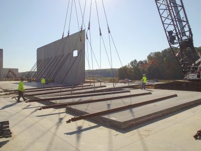Construction crew and crawler crane setting a precast concrete wall panel on a new slab